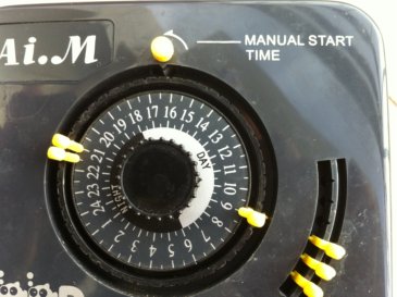 Close up of the clock, the yellow 'pegs' ensures food is dispensed at the hour its pegged to. The yellow knob on top allows for 'anytime' feeding by turning it.